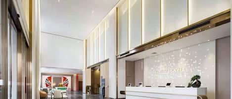A modern hotel lobby with a reception desk, seating area, and a large window.