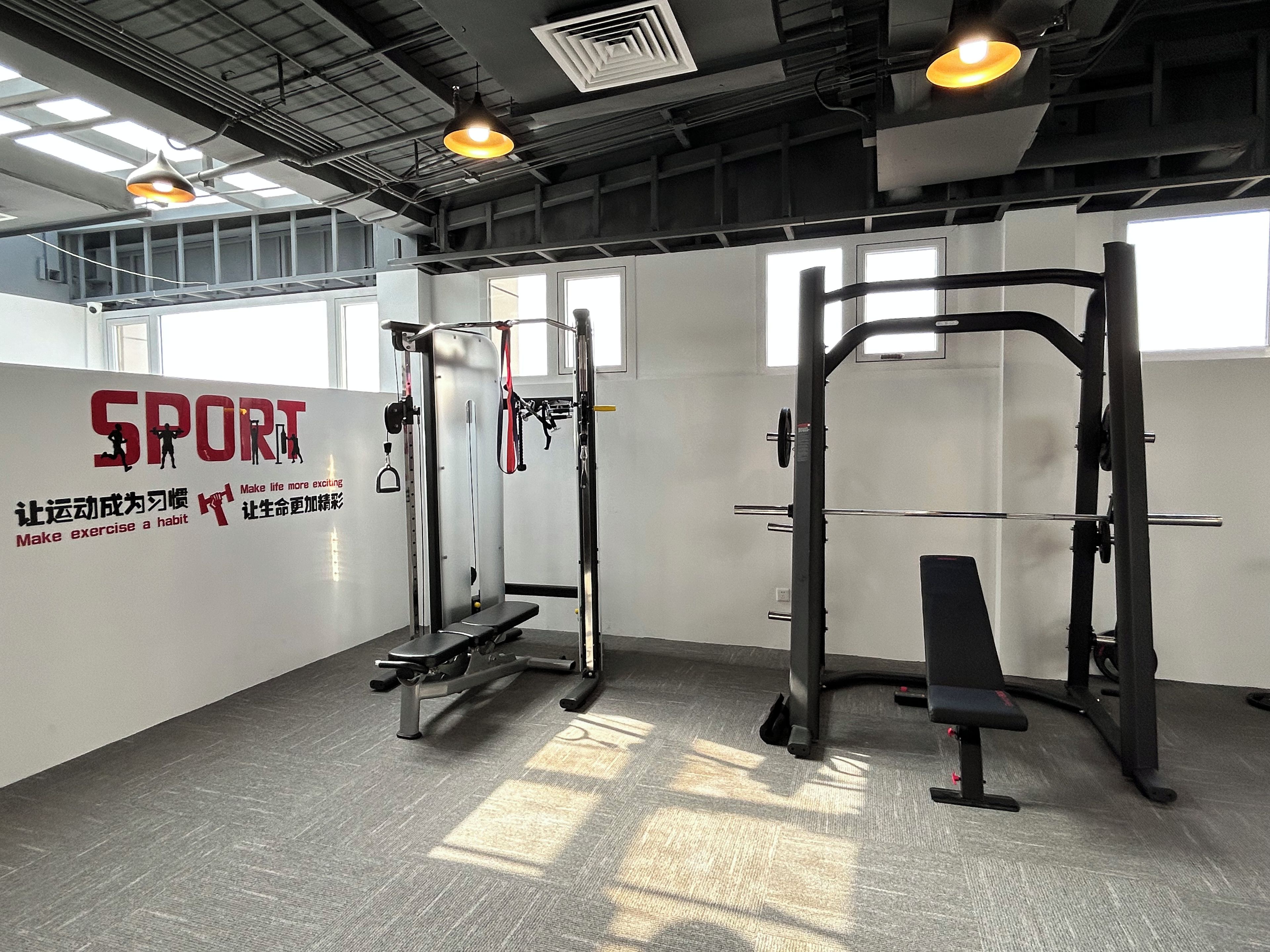A gym with exercise equipment, a wall with motivational text, and large windows allowing natural light.