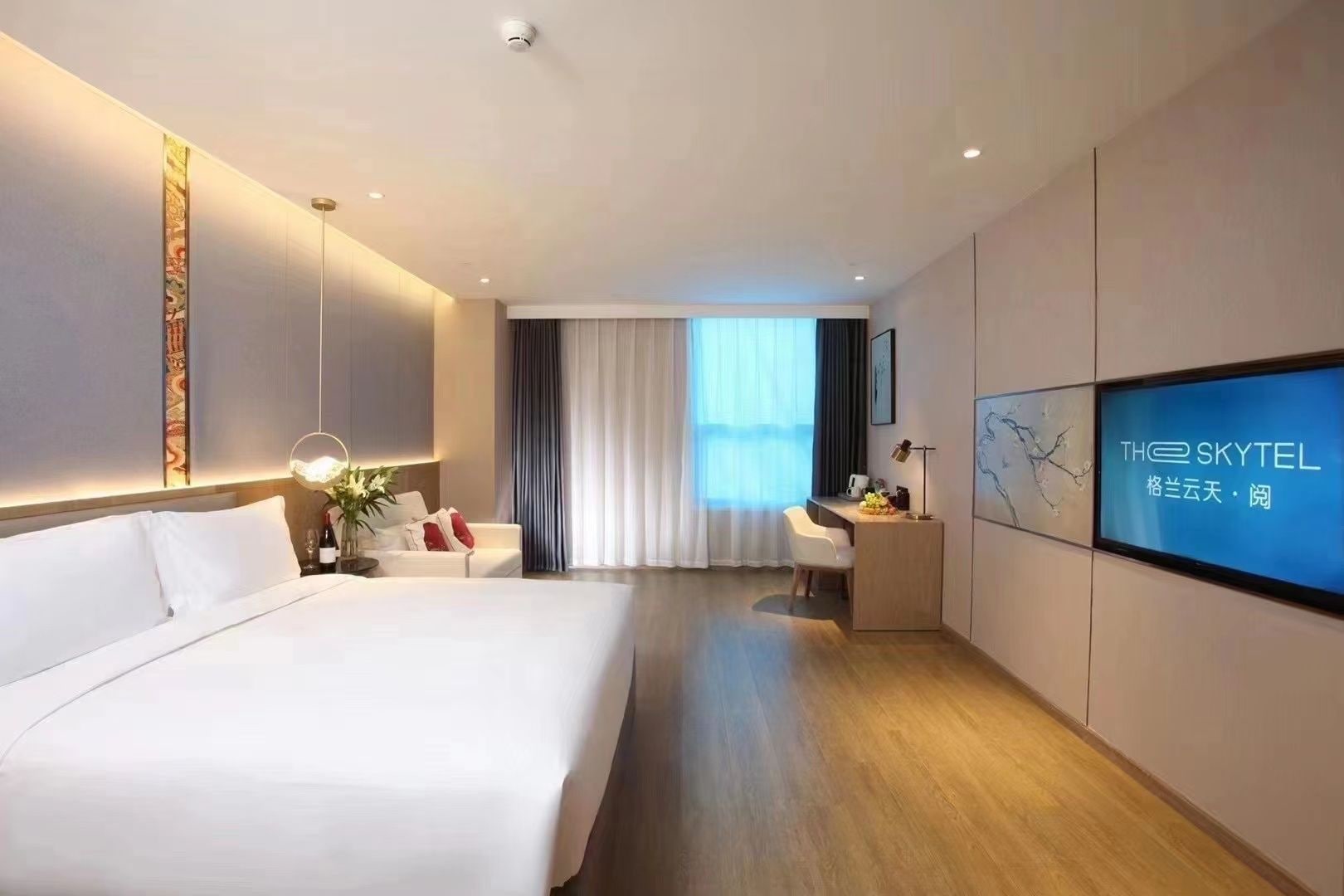 A hotel room with a large bed, a desk, a TV, and a view of the outdoors.