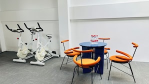 Quarto com duas bicicletas ergométricas, uma mesa redonda com cadeiras e uma garrafa de água sobre a mesa.