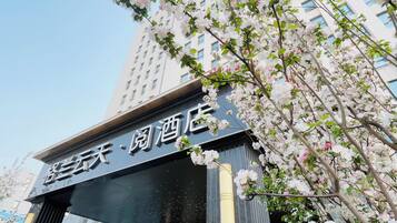 A hotel entrance with a sign in a foreign language, surrounded by blooming trees.