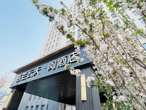 A hotel entrance with a sign in a foreign language, surrounded by blooming trees. - The Skytel Beijing Aoyu (Daxing)