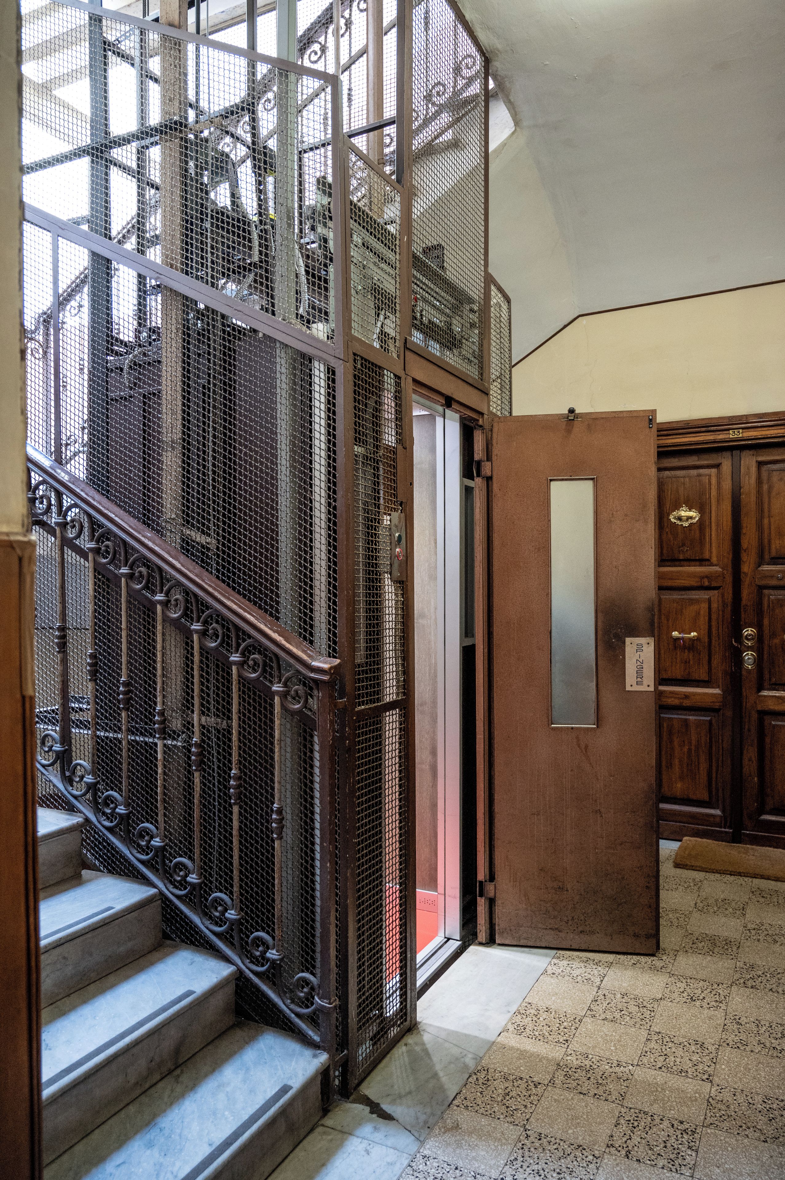Un intérieur à plusieurs niveaux, avec un escalier en métal, une porte en bois et un sol carrelé.
