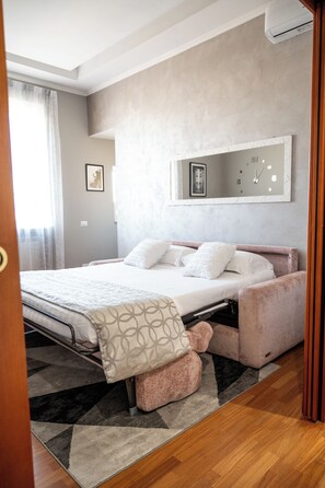 A bedroom with a bed, a bedside table, a mirror, and a window with curtains. - Vrbo Property (Roma)