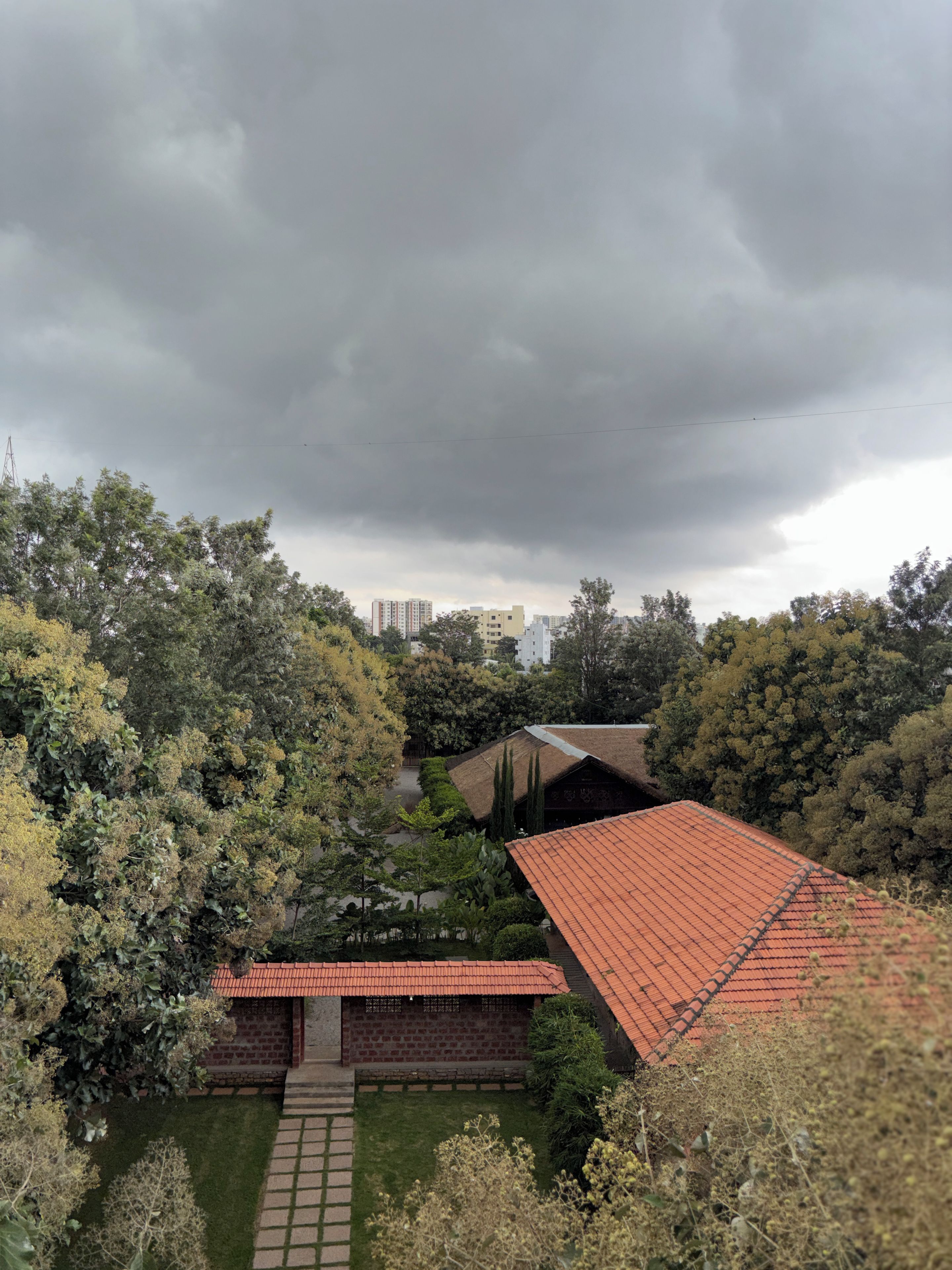 Ein Wohngebiet mit einem Ziegelgebäude und einem roten Ziegeldach, umgeben von üppiger Vegetation und einem bewölkten Himmel.
