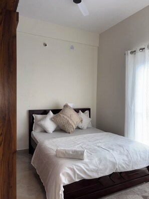 Quarto com cama, ventilador de teto e janela com cortinas.