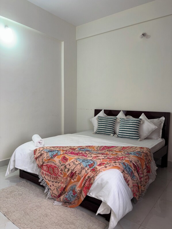 Uma cama bem arrumada com um edredom estampado, cabeceira com almofadas e um interruptor na parede.