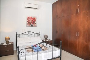 A bedroom with a bed, nightstands, a wardrobe, an air conditioner, and a floral painting. - The Goat House in Polis (Ppaphos)