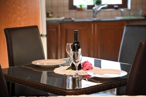 A dining table set with plates, a wine bottle, and glasses, with a kitchen in the background. - The Goat House in Polis (Ppaphos)