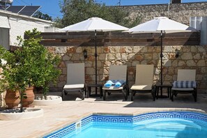 A poolside area with lounge chairs and umbrellas, a stone wall, and a tiled pool.