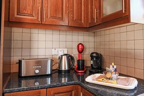 A kitchen with wooden cabinets, a toaster, a kettle, a coffee maker, and a tray with bread and condiments. - The Goat House in Polis (Ppaphos)