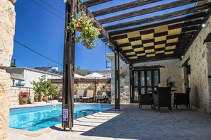 A covered outdoor area with a pool, outdoor seating, and a stone wall.