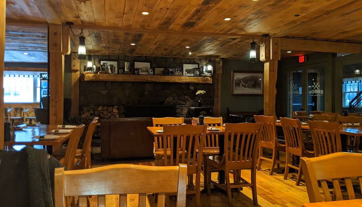 A restaurant interior with wooden furniture, a stone fireplace, and framed pictures on the walls.