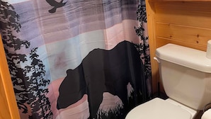 A bathroom with a patterned shower curtain, a toilet, and a window with blinds. - Delightful 2-bedroom Tiny home with AC/Heat in Tamworth (Tamworth)