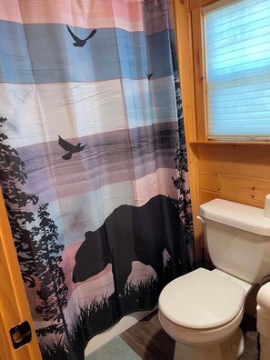 Un baño con cortina de ducha estampada, inodoro y ventana con persianas.