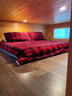 Un dormitorio con cama, techo de madera y una ventana.