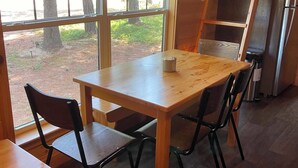 A wooden interior with a table and chairs, a refrigerator, and a window with a view of trees. - Delightful 2-bedroom Tiny home with AC/Heat in Tamworth (Tamworth)