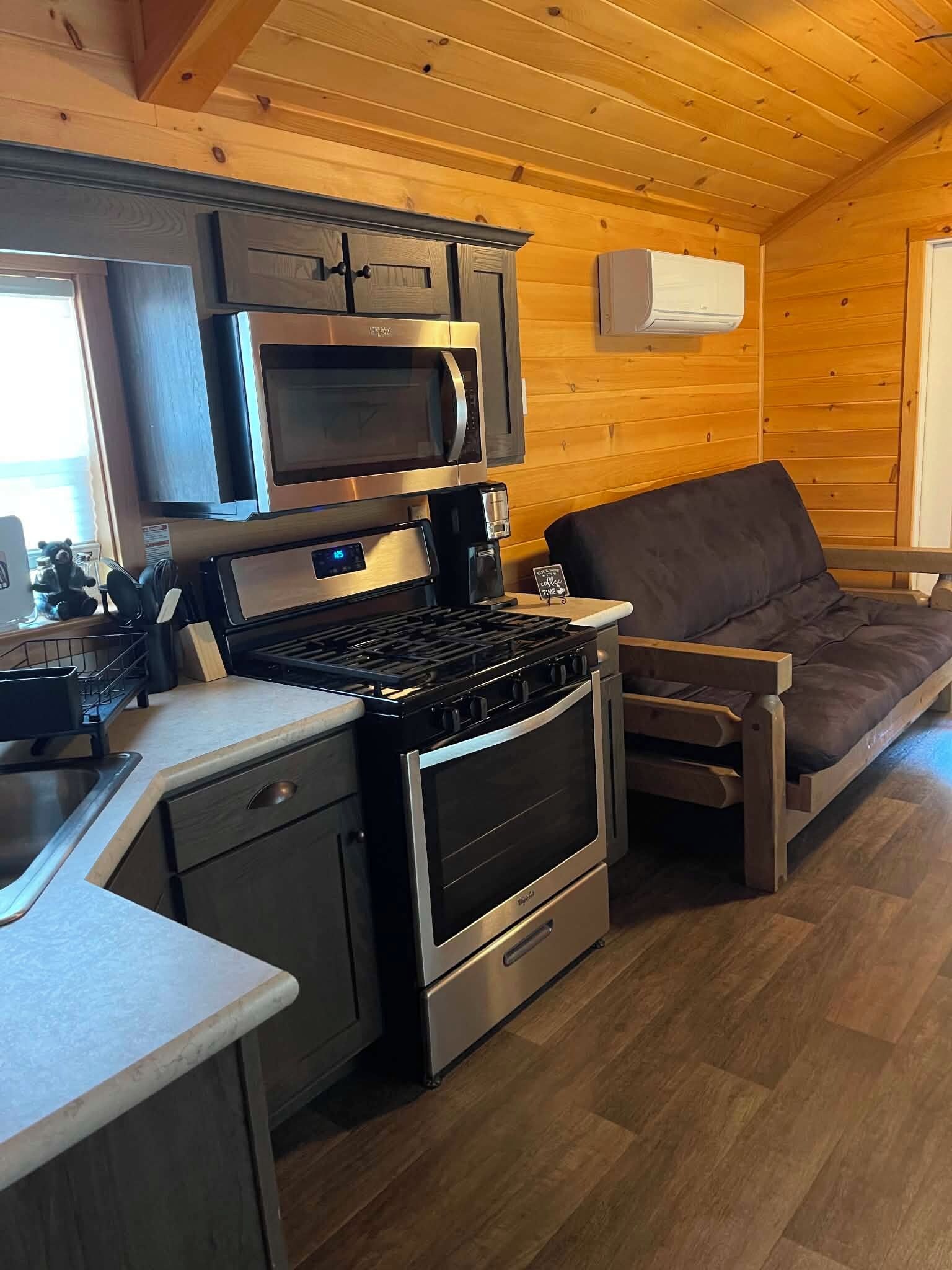 Una cocina compacta con microondas, estufa y horno, un lavamanos pequeño y una zona de comedor de madera.