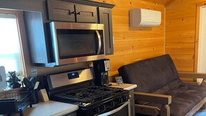 A compact kitchen with a microwave, stove, and oven, a small countertop, and a wooden floor. - Delightful 2-bedroom Tiny home with AC/Heat in Tamworth (Tamworth)