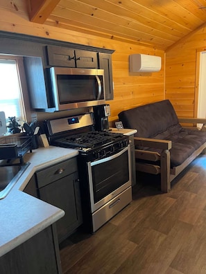 Una cocina compacta con microondas, estufa y horno, una pequeña encimera y suelo de madera.