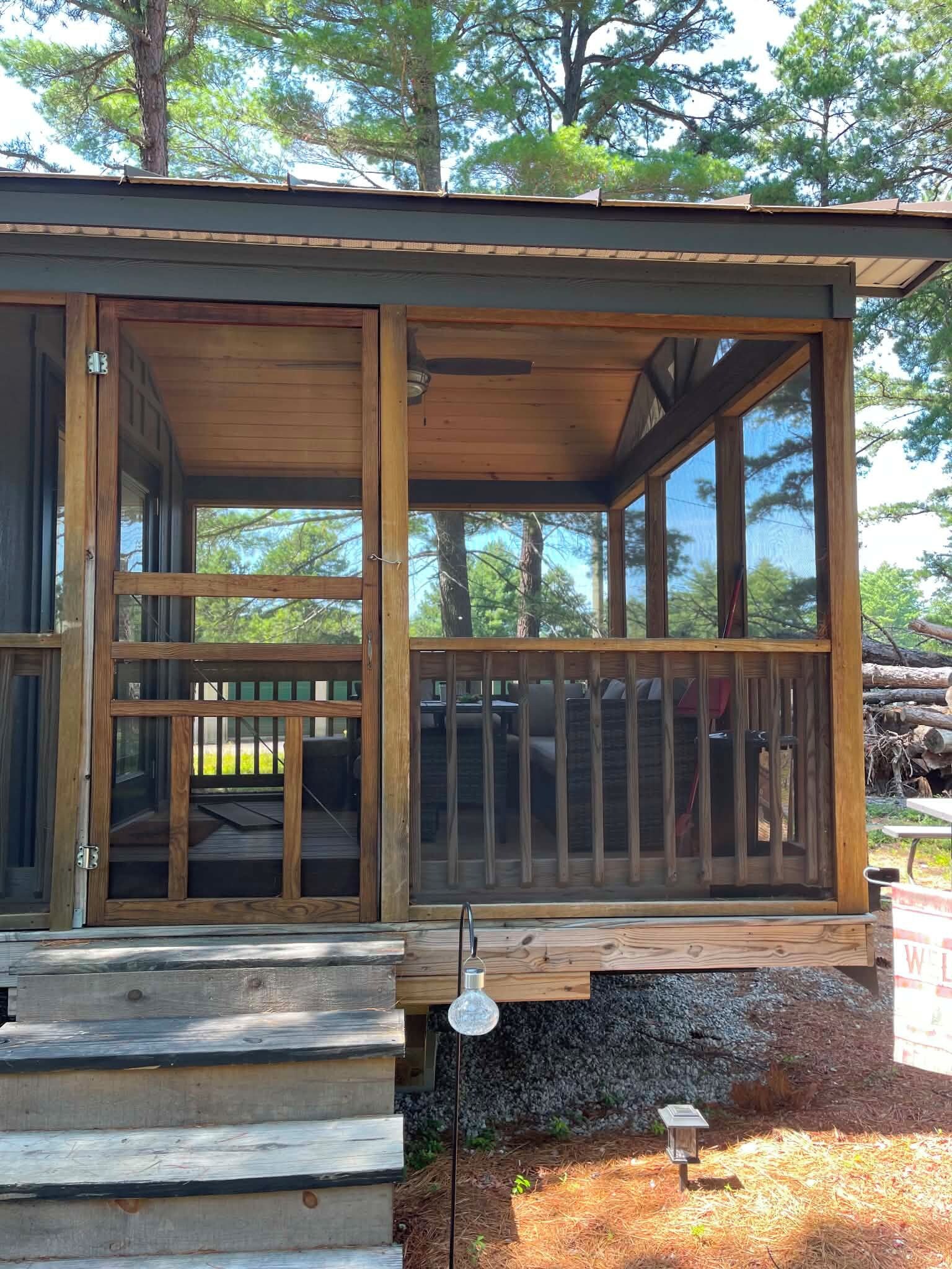 Une cabane en bois dotée d’un porche couvert, d’un escalier apparent et d’un petit espace extérieur agrémenté d’une pancarte de bienvenue.