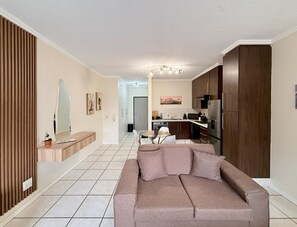 A modern living room with a sofa, a dining table, and a kitchen area in the background. - Marvelous 1-bedroom apartment in Sandton perfect for your stay (Sandton)