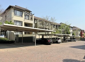 A residential building with a covered parking area and multiple cars parked. - Marvelous 1-bedroom apartment in Sandton perfect for your stay (Sandton)