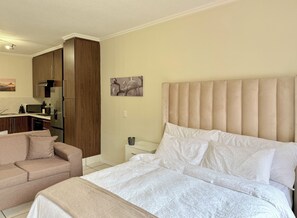 Quarto com cama, sofá, cozinha compacta e banheiro.