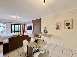 Habitación de hotel moderna con cama, televisor, zona de comedor con mesa y sillas, y obras de arte en las paredes.
