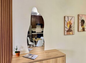 Una cocina moderna con gabinetes de madera, una campana de acero inoxidable y una zona de comedor con mesa de vidrio y sillas blancas.
