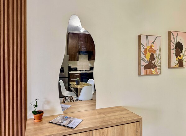 Cozinha moderna com armários de madeira, coifa de aço inoxidável e área de refeições com mesa de vidro e cadeiras brancas.