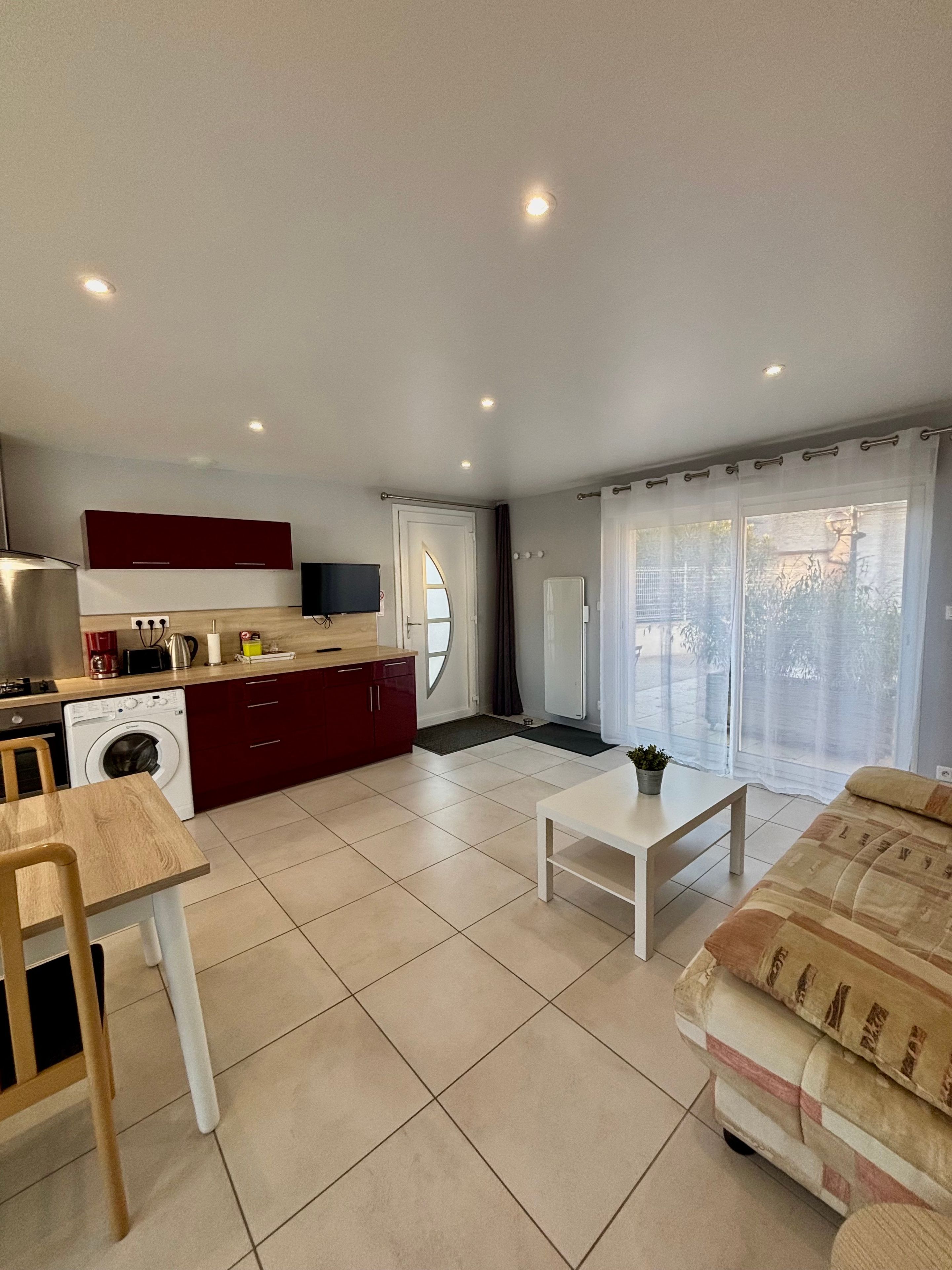 A modern kitchen with a washing machine, a dining table, and a sofa in a living area with a large window.
