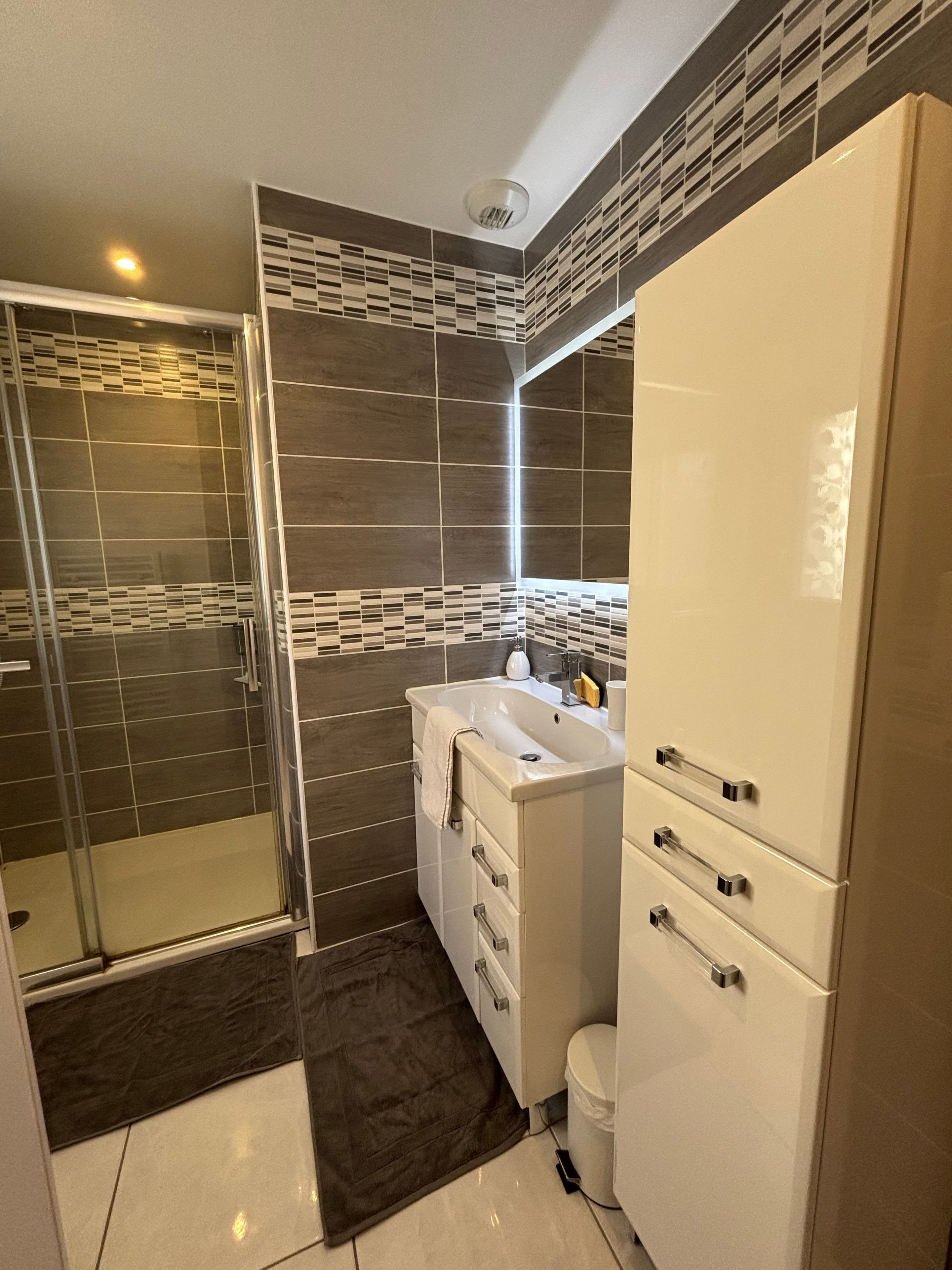 Une salle de bain moderne avec une douche à parois de verre, un lavabo blanc et un meuble avec des tiroirs.