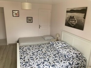Un dormitorio con cama, una puerta, una lámpara y dos cuadros en la pared.