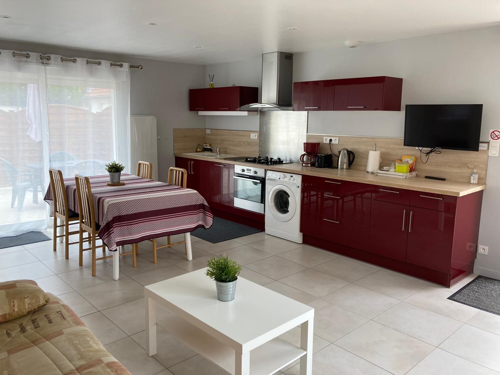 Une cuisine compacte équipée d’une cuisinière, d’un four et d’un lave-linge, un coin repas avec une table et des chaises, et un téléviseur fixé au mur.