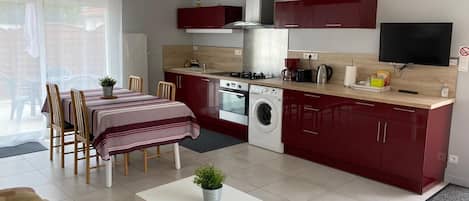 A compact kitchen with a stove, oven, and washing machine, a dining area with a table and chairs, and a TV mounted on the wall.