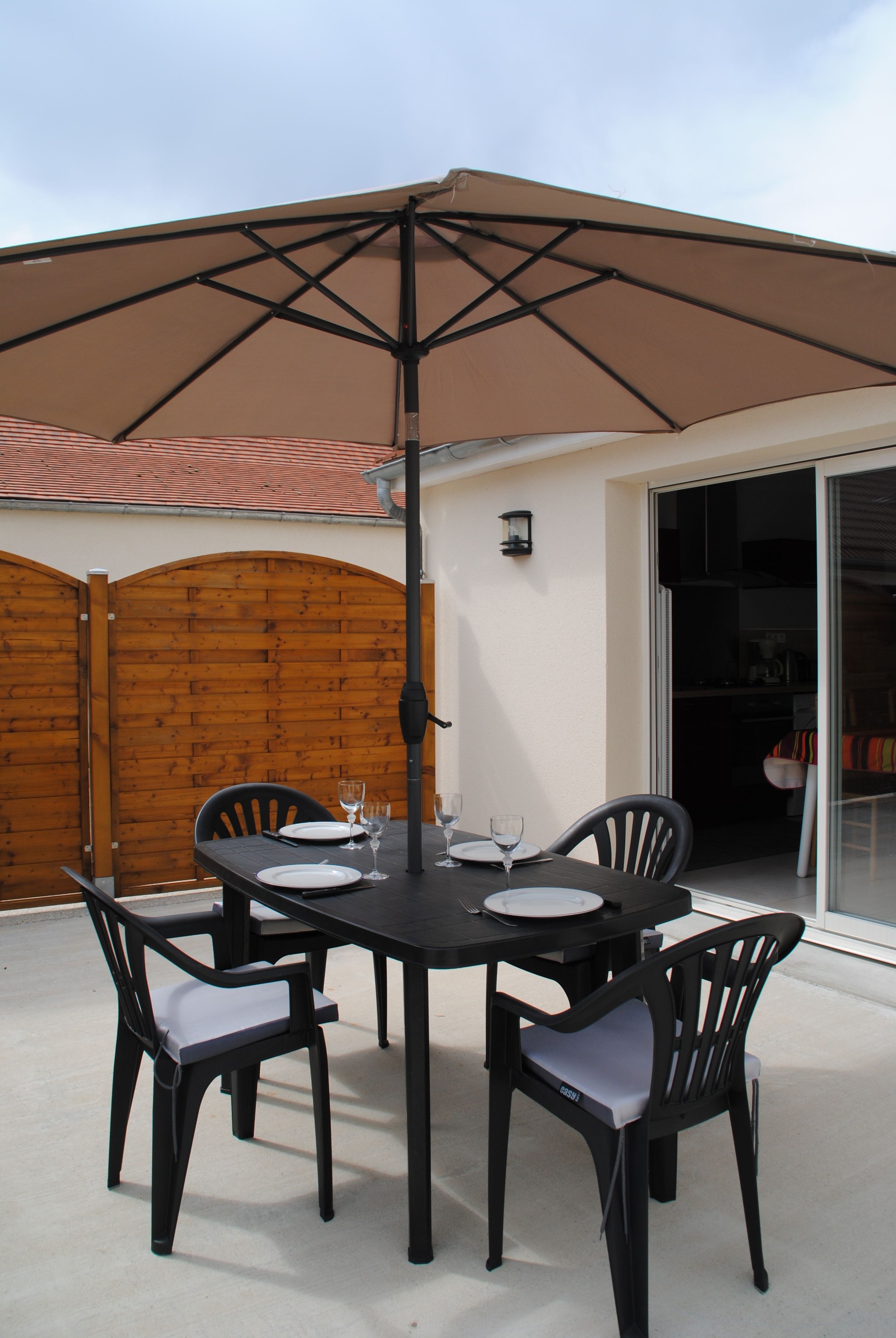 An outdoor patio with a table and chairs, a large umbrella, and a wooden fence.