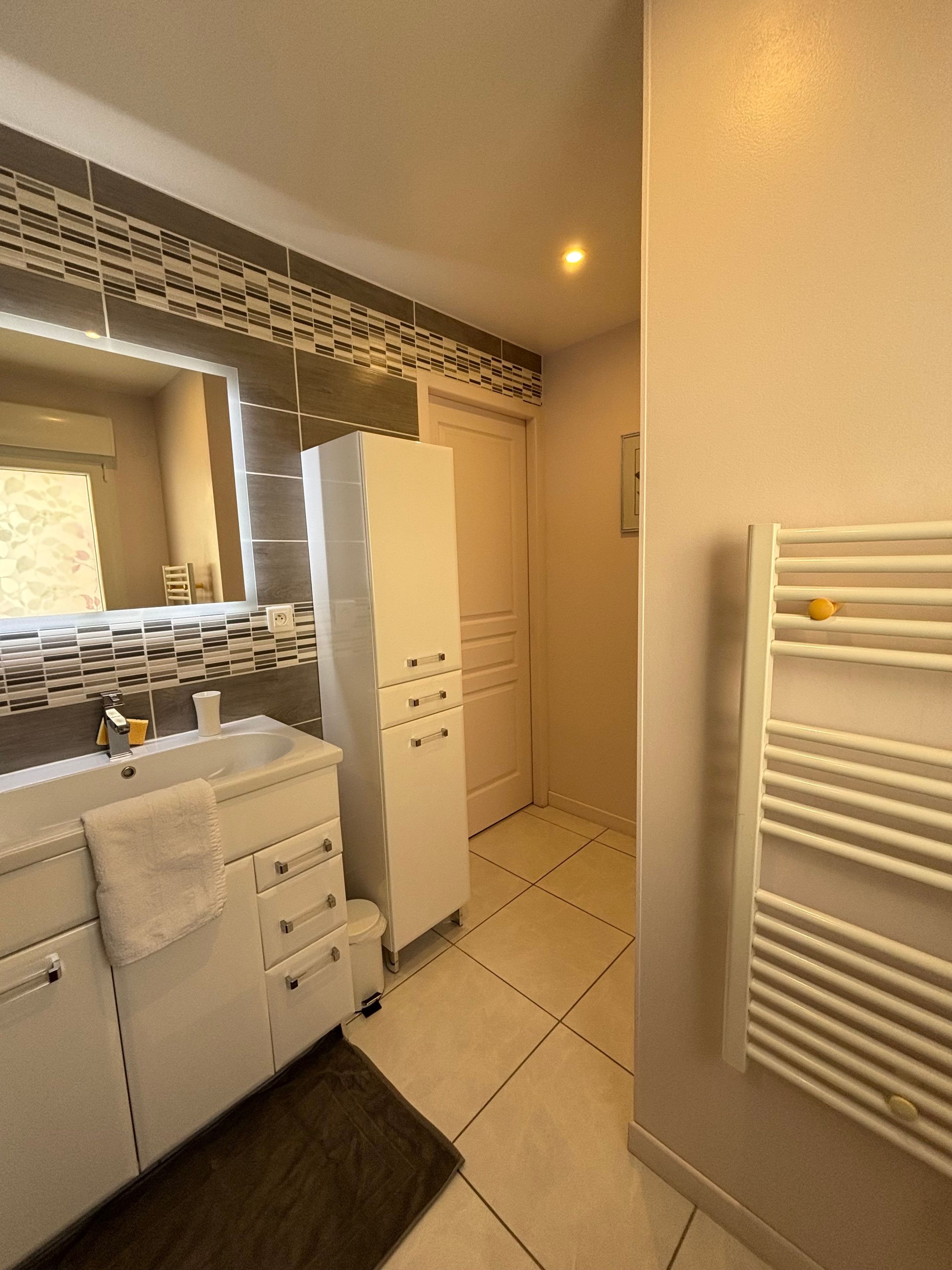 Une salle de bain moderne avec un lavabo blanc, un miroir et des armoires.