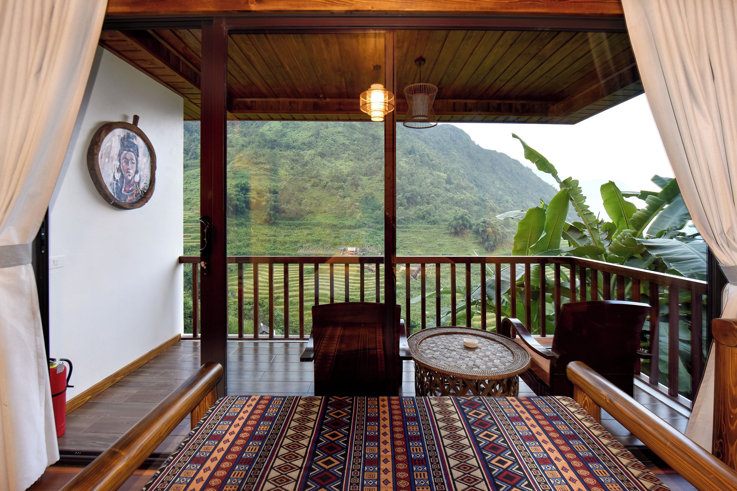 A balcony with a patterned floor, wooden furniture, and a view of a mountainous landscape.