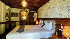 A hotel room with a large bed, wooden headboard, stone wall, and a small desk with a lamp. - MAISON DE LAO CHAI (Sa Pa)