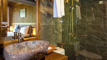 Een badkamer met een ruime stenen wasbak, een houten wastafelmeubel, een douche met glazen wanden en een houten hoofdbord.