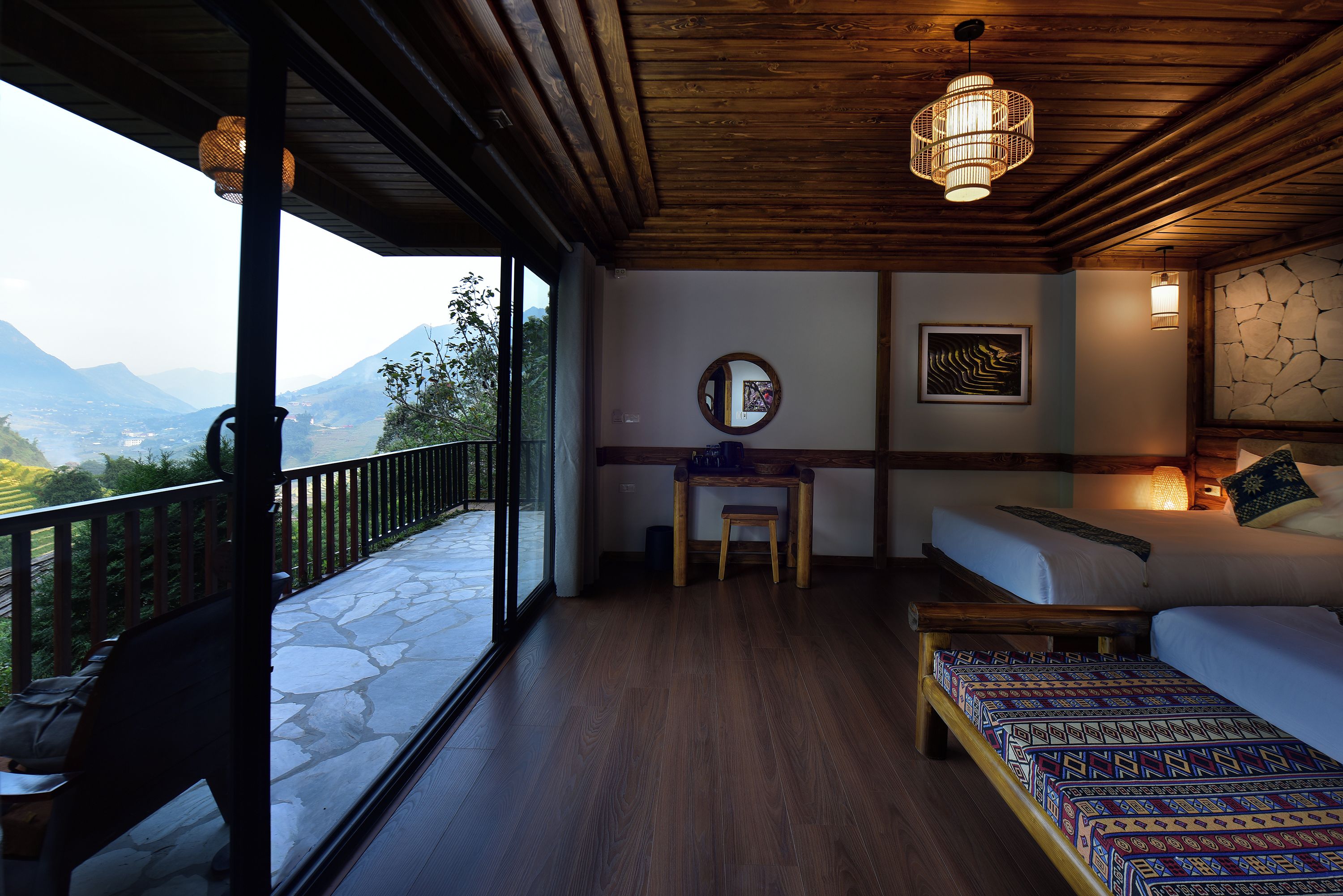 A room with a balcony, a bed, a desk, and a view of mountains.
