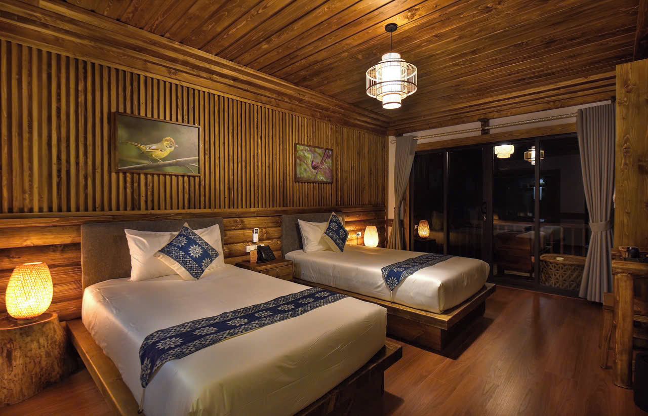 A room with two beds, wooden paneling, a painting, and a chandelier.