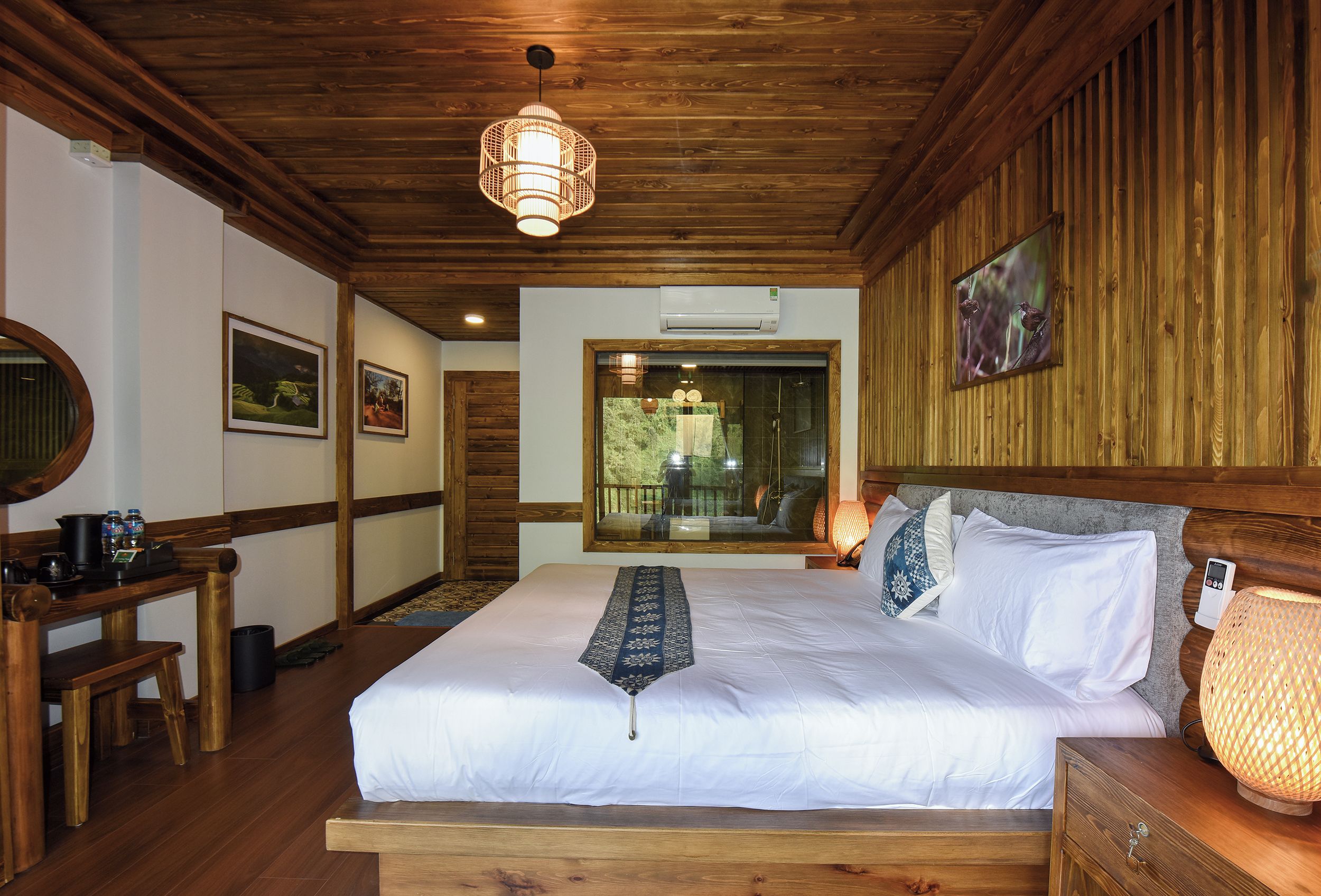 A wooden-paneled room with a bed, a desk, and a window with a view of trees.