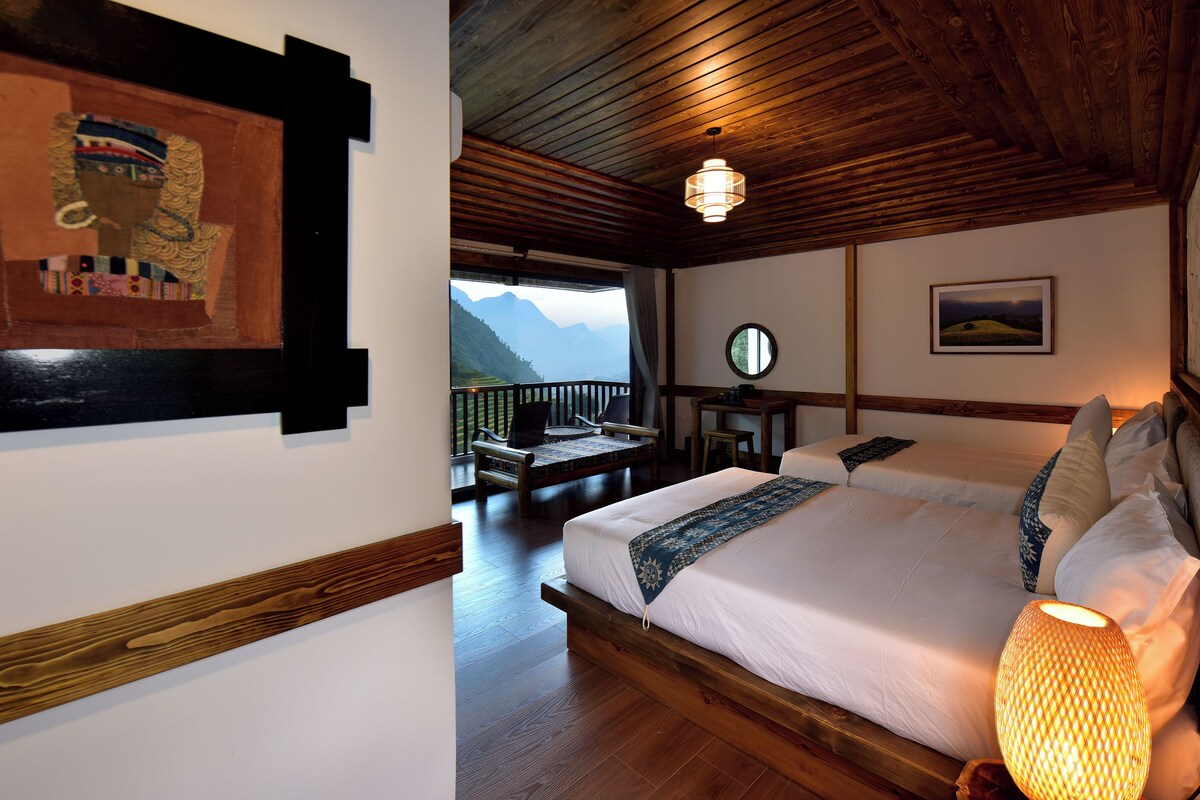 Quarto com uma cama grande, teto de madeira e vista para montanhas.