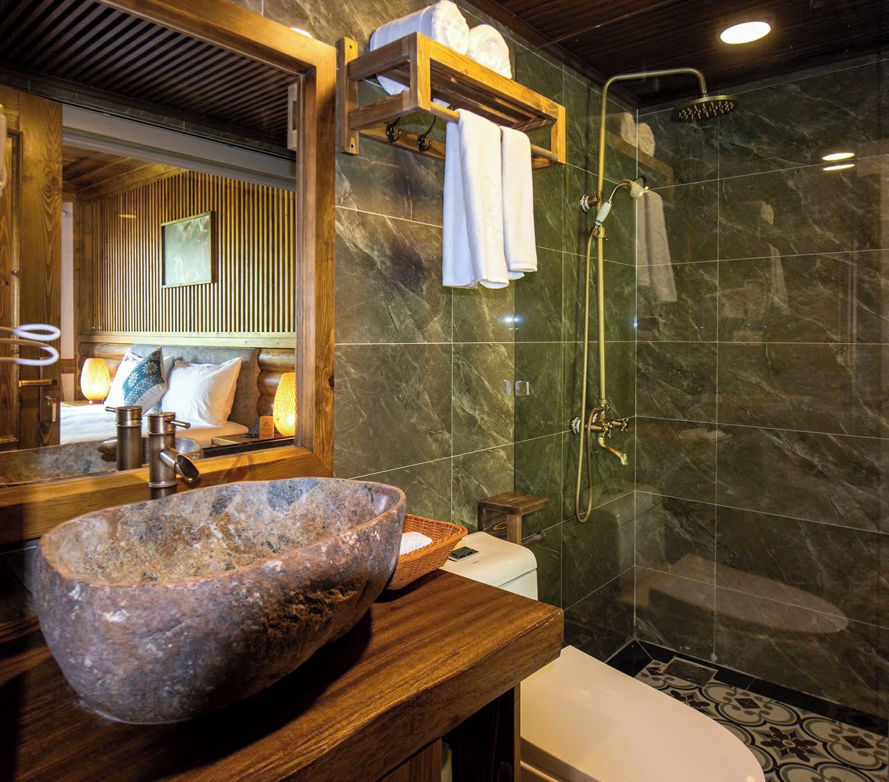 A bathroom with a large stone basin, a wooden vanity, a glass-enclosed shower, and a wooden shelf with towels.
