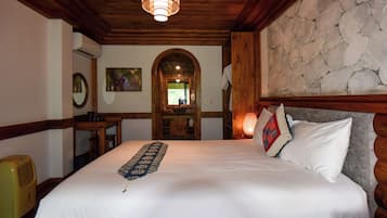 Une chambre d’hôtel avec un grand lit, une tête de lit en bois, un mur en pierre, un plafond en bois, une petite table avec une lampe et un tableau accroché au mur.