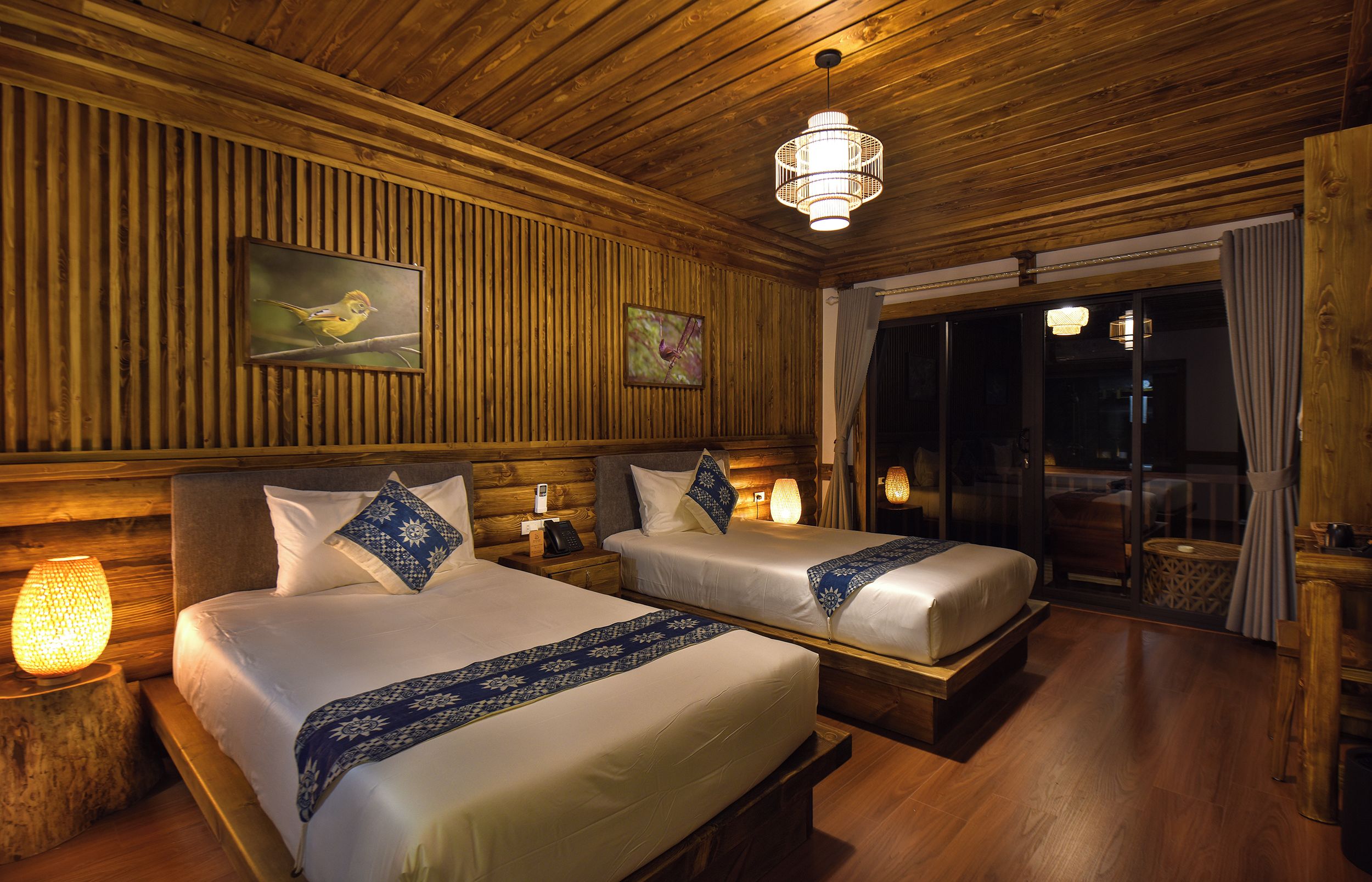 A hotel room with two beds, wooden paneling, a chandelier, and a large window with curtains.