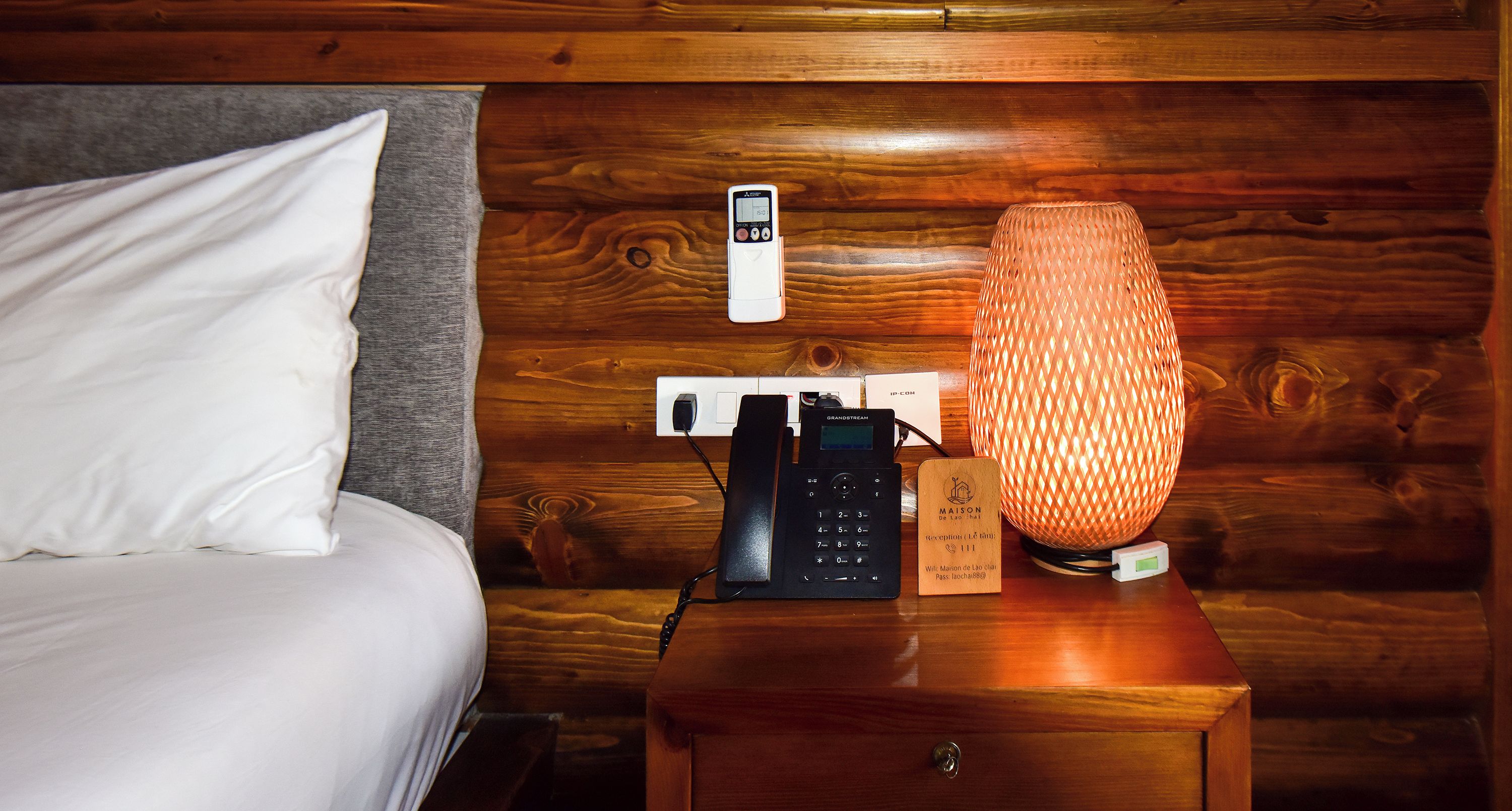 Une table de chevet en bois avec une lampe, un téléphone et un symbole Wi-Fi.