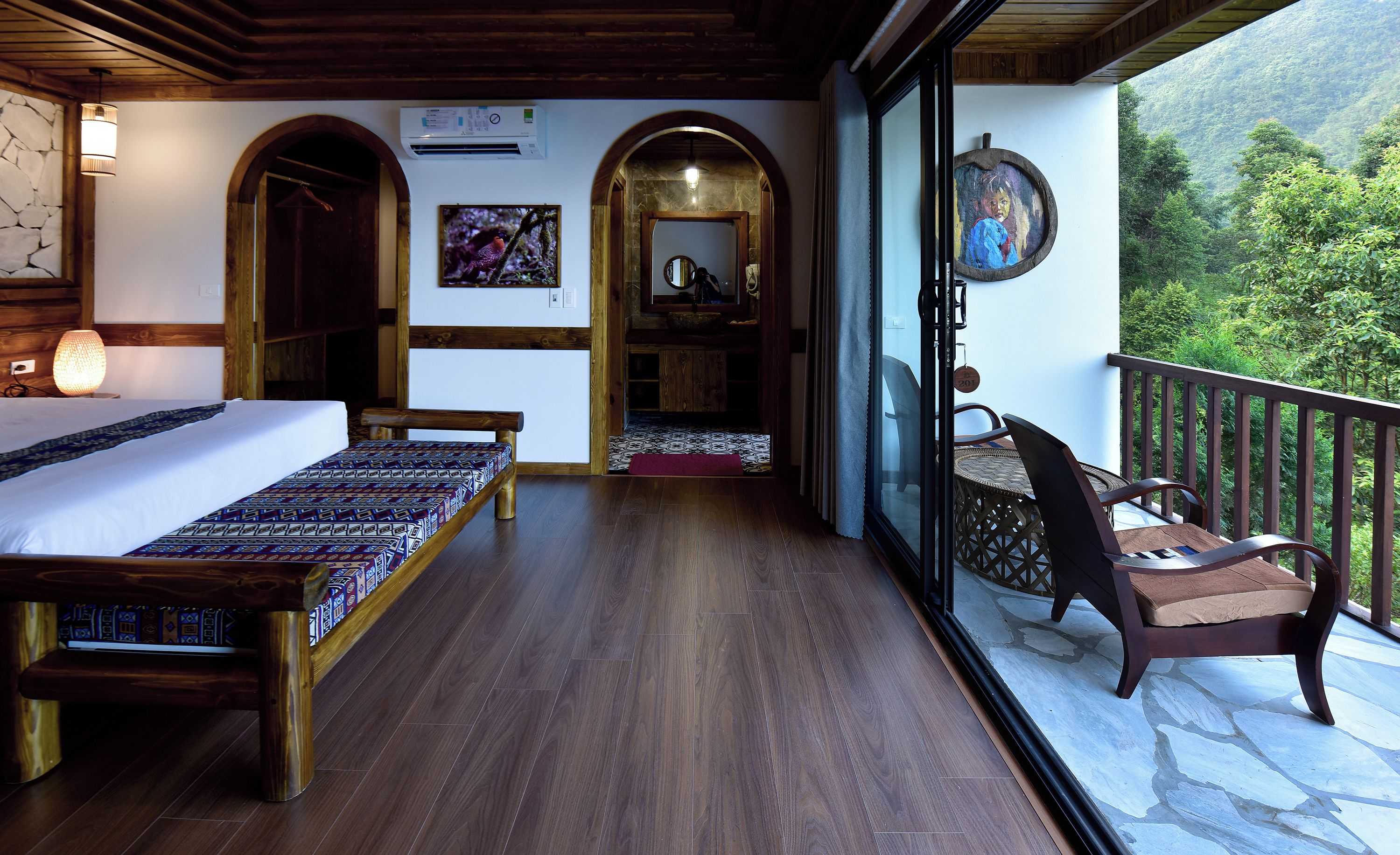 A balcony with a bed, a chair, and a view of a forested hillside.